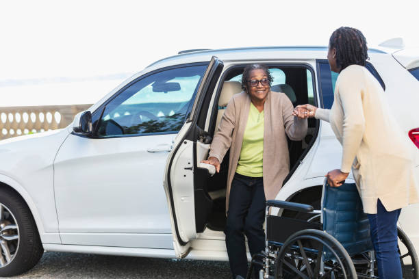 Driver helping a senior woman step out of an SUV with a wheelchair nearby